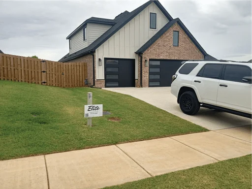 Elite Garage Door Services of Northwest ArkansasA modern home in NWA with black residential garage doors is shown. A white SUV is parked in the driveway. A sign for Elite Garage Door highlights local, reliable garage door service, emphasizing quality and professionalism for homeowners.