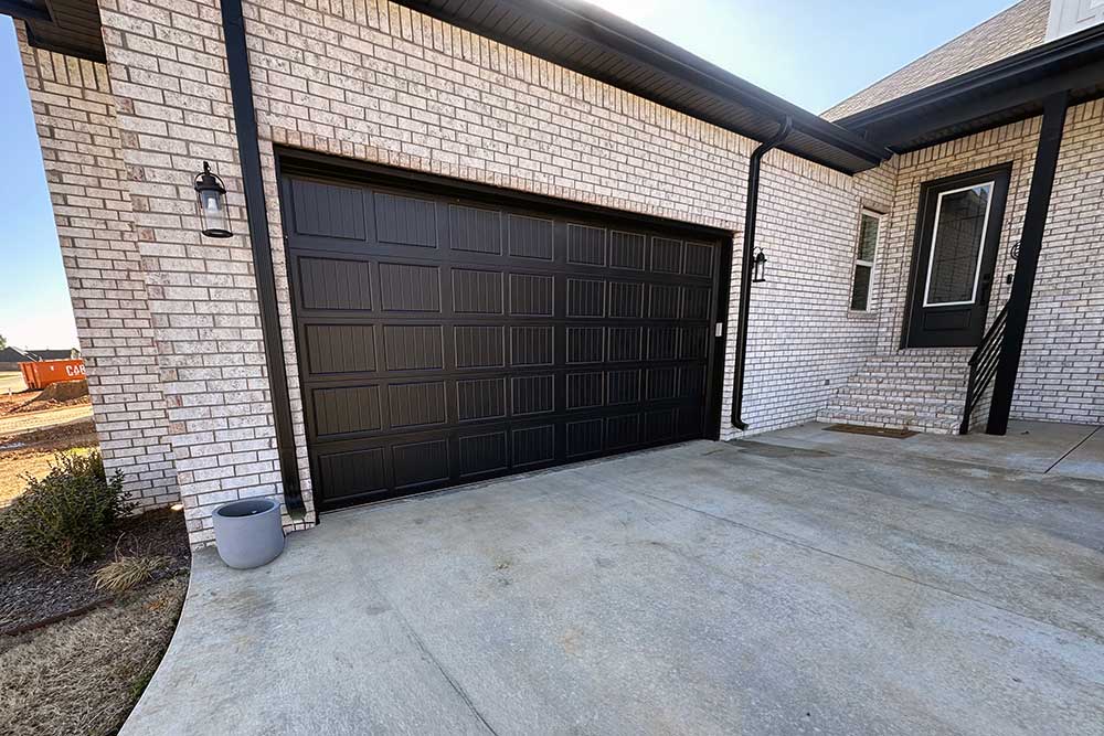 bella-vista-image Elite Garage Door Services of Northwest Arkansas-A black residential garage door is installed on a white brick house in Northwest Arkansas, showcasing professional garage door installation services available in the area.