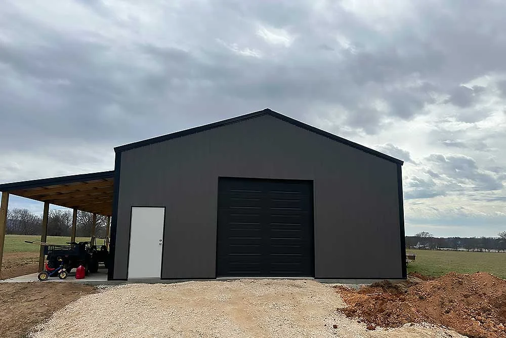 Elite Garage Door Services of Northwest Arkansas-A large black building with a closed overhead garage door under a cloudy sky, surrounded by rural land. This structure is typical in Northwest Arkansas,…