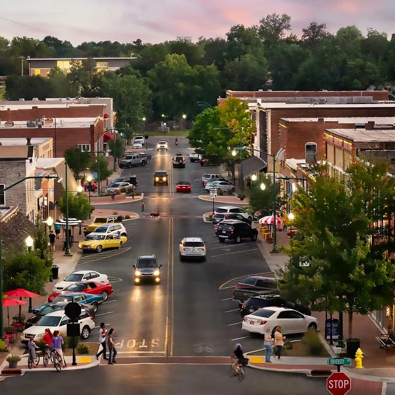 Elite Garage Door Services of Northwest Arkansas-Scenic view of a bustling downtown street in Bentonville, AR, during sunset, with cars and pedestrians. The vibrant atmosphere reflects the local charm of Northwest Arkansas, a region known for professional and reliable garage door services.