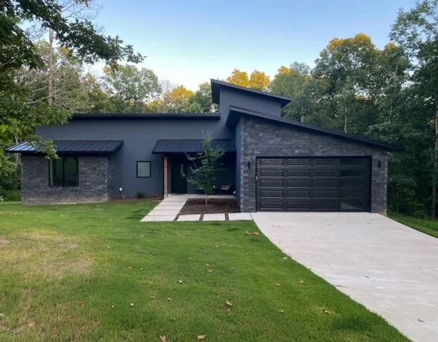 Elite Garage Door Services of Northwest ArkansasModern gray house with sleek black residential garage doors in a lush green setting, showcasing local architecture in Northwest Arkansas. Ideal for those seeking a reliable garage door service for their home in Rogers, AR.
