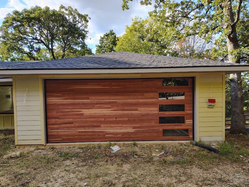Elite Garage Door Services of Northwest ArkansasA newly installed wooden residential garage door with horizontal windows in a yellow house, surrounded by trees, showcasing a professional garage door installation in Northwest Arkansas.