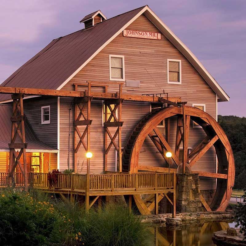 Elite Garage Door Services of Northwest Arkansas-A historic mill with a large wooden waterwheel at sunset, surrounded by lush greenery. This picturesque scene is reminiscent of the charming landscapes found in Northwest Arkansas, highlighting the local beauty and serene environment.
