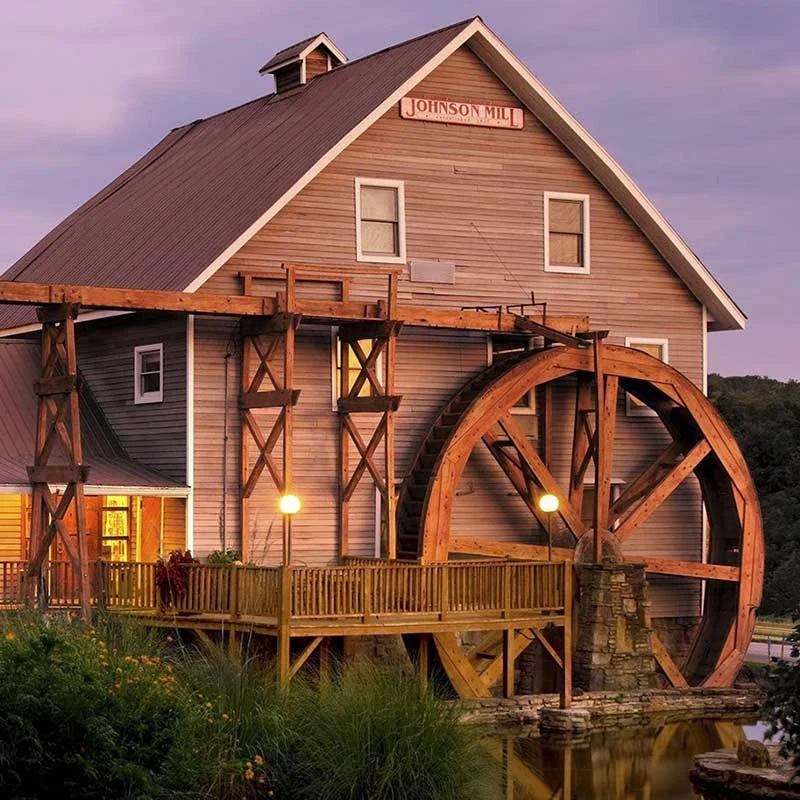 Elite Garage Door Services of Northwest Arkansas-A historic mill with a large wooden waterwheel at sunset, surrounded by lush greenery. This picturesque scene is reminiscent of the charming landscapes found in Northwest Arkansas, highlighting the local beauty and serene environment.