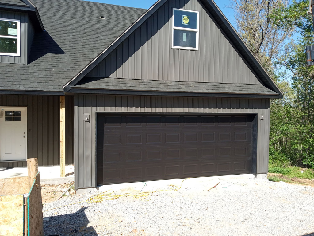 Elite Garage Door Services of Northwest ArkansasA newly installed black residential garage door on a gray house in Northwest Arkansas, highlighting professional garage door installation services available in Bentonville AR.