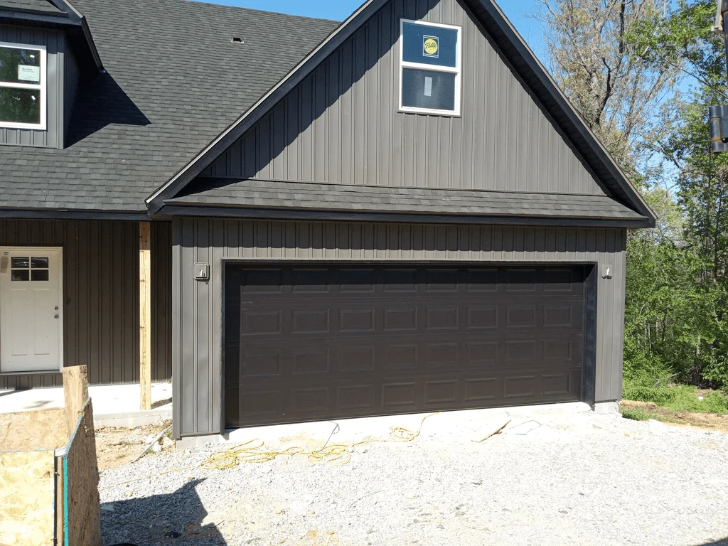 Elite Garage Door Services of Northwest ArkansasA newly installed black residential garage door on a gray house in Northwest Arkansas, highlighting professional garage door installation services available in Bentonville AR.