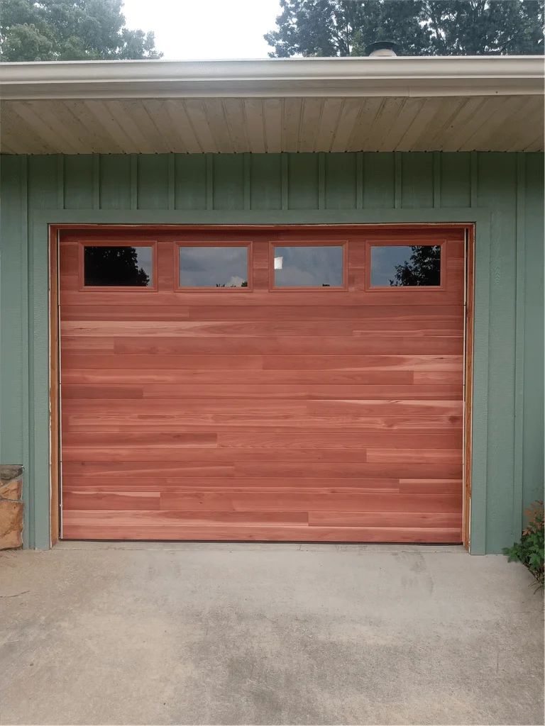 Elite Garage Door Services of Northwest ArkansasA newly installed, modern wooden residential garage door with windows at the top, located in Northwest Arkansas, showcasing reliable garage door service for homeowners in the area.