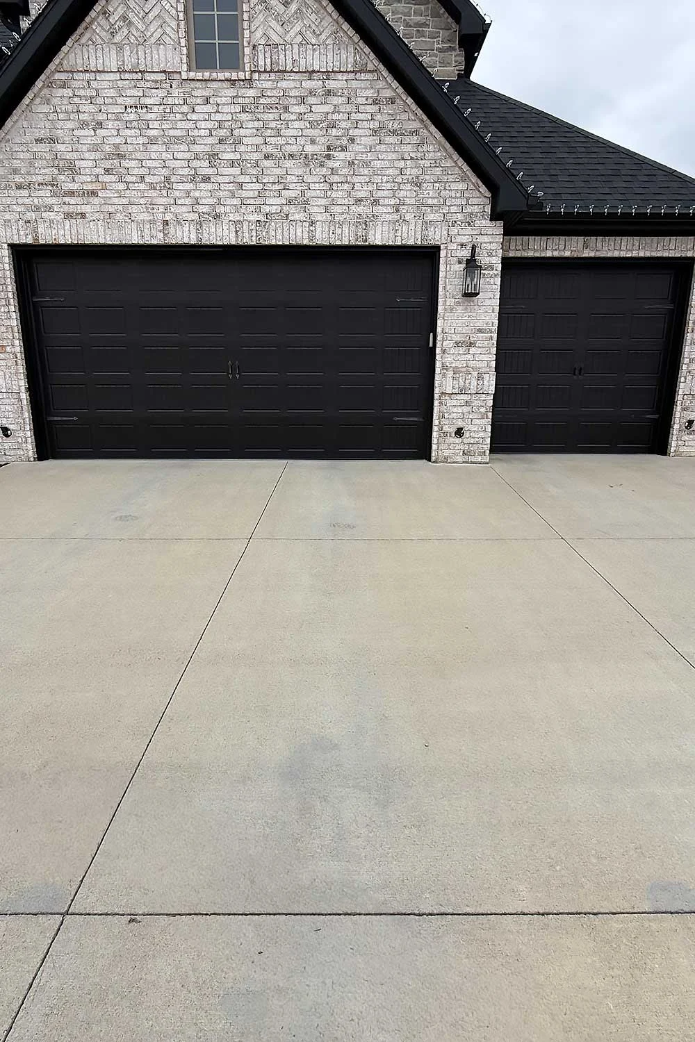 Elite Garage Door Services of Northwest Arkansas-A beautiful residential brick home with three sleek black garage doors, showcasing professional garage door installation in Northwest Arkansas.