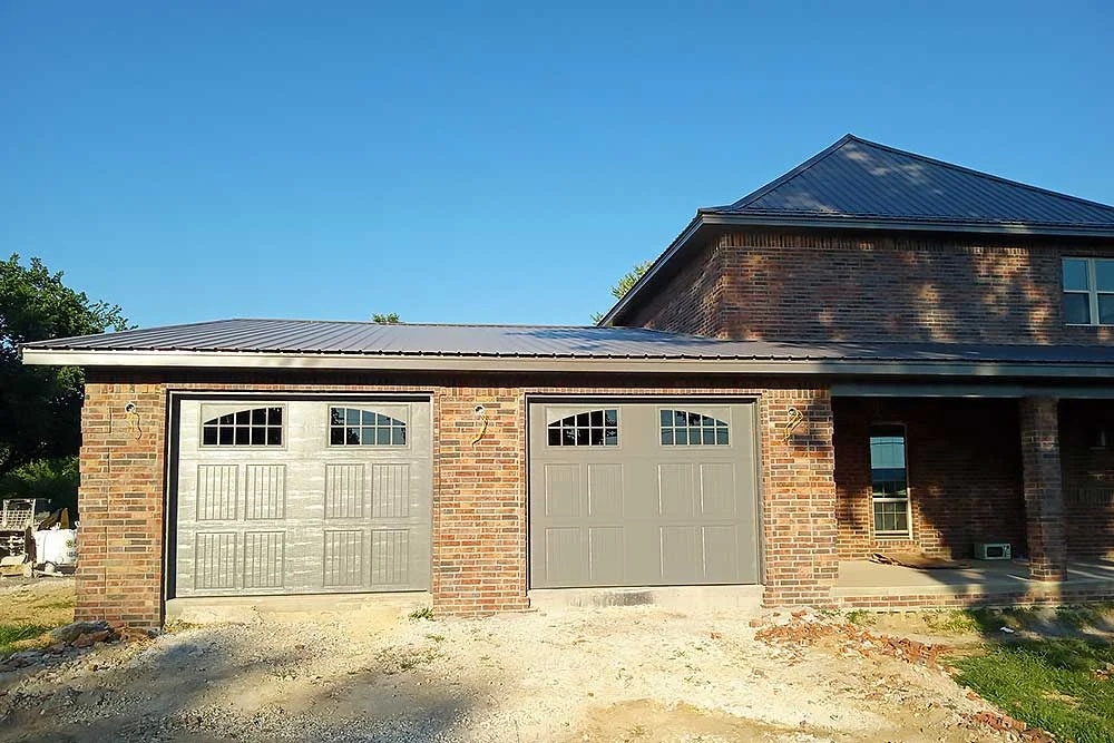 Elite Garage Door Services of Northwest Arkansas-A brick house in Northwest Arkansas with two newly installed residential garage doors under a clear blue sky, showcasing local garage door service expertise.