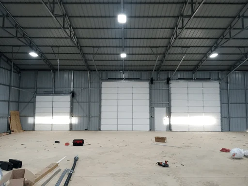 Elite Garage Door Services of Northwest ArkansasA spacious warehouse with three large overhead garage doors partially open, tools scattered on the floor. This setting in Northwest Arkansas highlights the need for professional garage door service and installation.