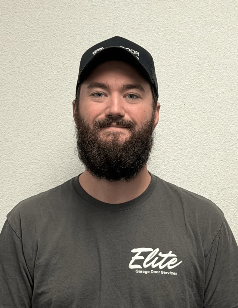 Elite Garage Door Services of Northwest ArkansasA professional technician from Elite Garage Door Services in Northwest Arkansas stands against a light wall, wearing a branded cap and shirt, symbolizing reliable local…