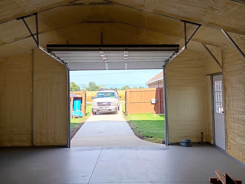 work-carousel-3 Elite Garage Door Services of Northwest Arkansas-View from inside a garage with an open overhead garage door, showing a driveway and a parked truck outside under a clear sky. This image highlights professional garage door service available in Northwest Arkansas.