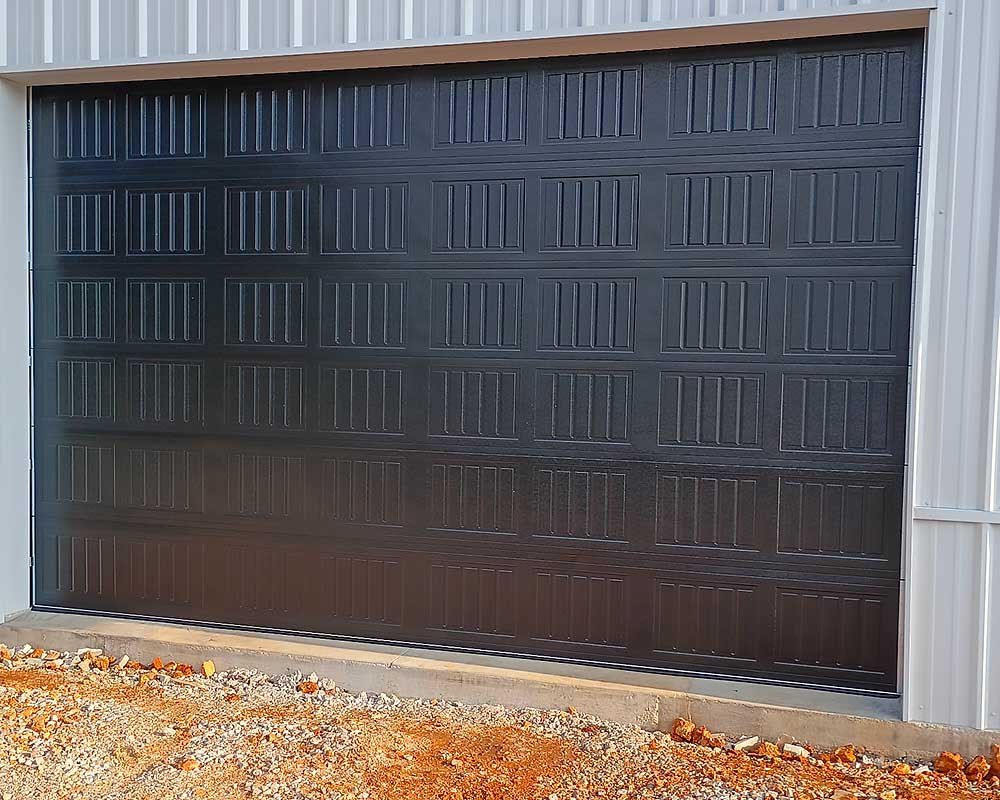 work-carousel-7 Elite Garage Door Services of Northwest Arkansas-A newly installed black overhead garage door is shown against a white metal building, demonstrating professional garage door installation services in Northwest Arkansas.